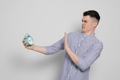 Emotional young man with alarm clock on light grey background. Being late concept