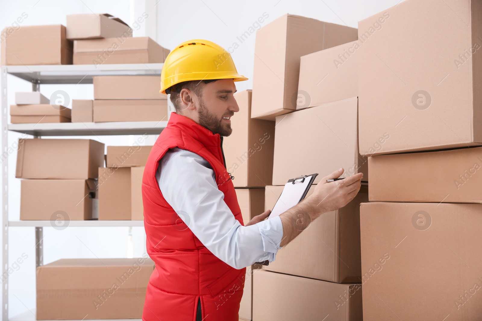 Photo of Young man with clipboard near cardboard boxes at warehouse