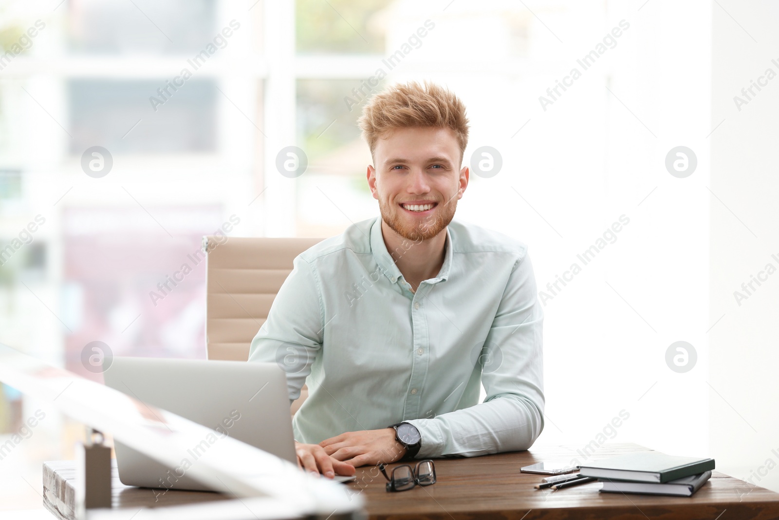 Photo of Portrait of handsome young man sitting at desk in office