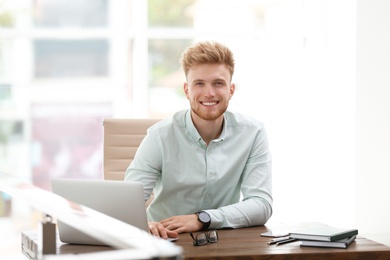 Photo of Portrait of handsome young man sitting at desk in office