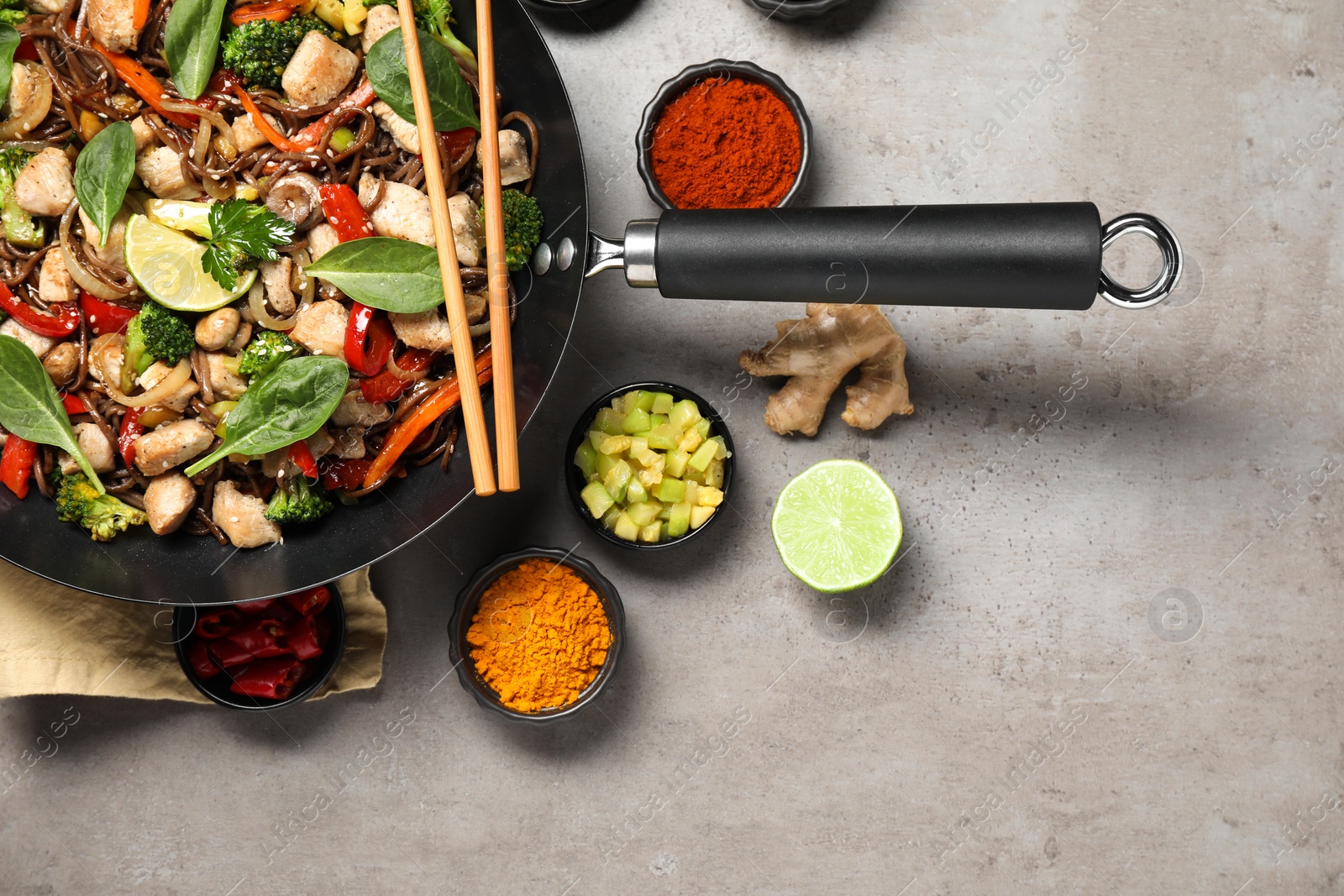 Photo of Stir-fry. Tasty noodles with meat in wok, chopsticks and ingredients on grey textured table, flat lay