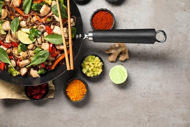 Photo of Stir-fry. Tasty noodles with meat in wok, chopsticks and ingredients on grey textured table, flat lay