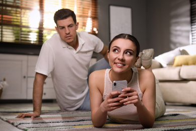Photo of Distrustful man peering into girlfriend's smartphone at home. Jealousy in relationship