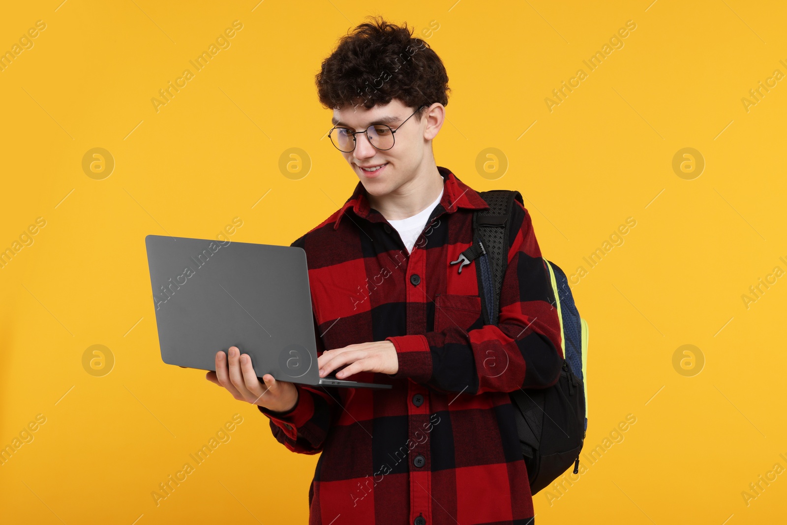 Photo of Portrait of student with backpack, laptop and glasses on orange background