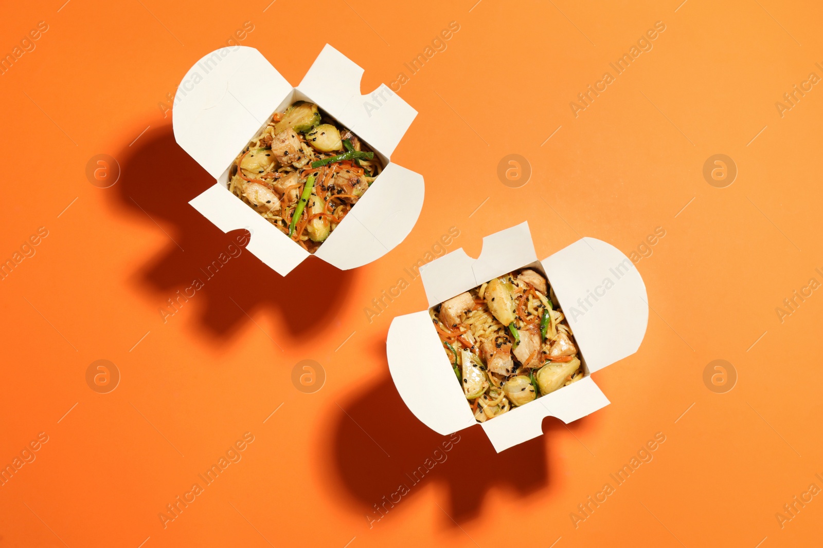 Photo of Boxes of noodle wok on orange background, flat lay