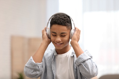 Photo of African-American teenage boy listening to music with headphones at home