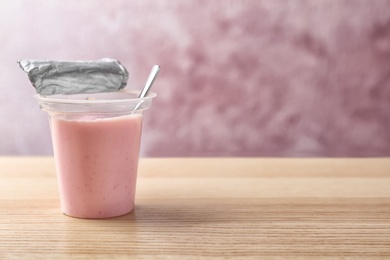 Plastic cup with tasty yogurt on wooden table