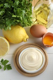 Photo of Fresh mayonnaise sauce in bowl and ingredients on white wooden table, flat lay