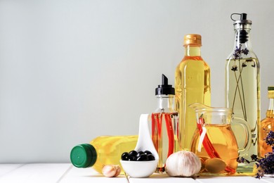 Photo of Different cooking oils and ingredients on white wooden table against grey background, space for text