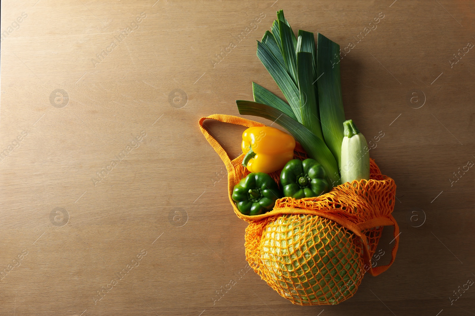 Photo of Different fresh vegetables in eco mesh bag on wooden table, top view