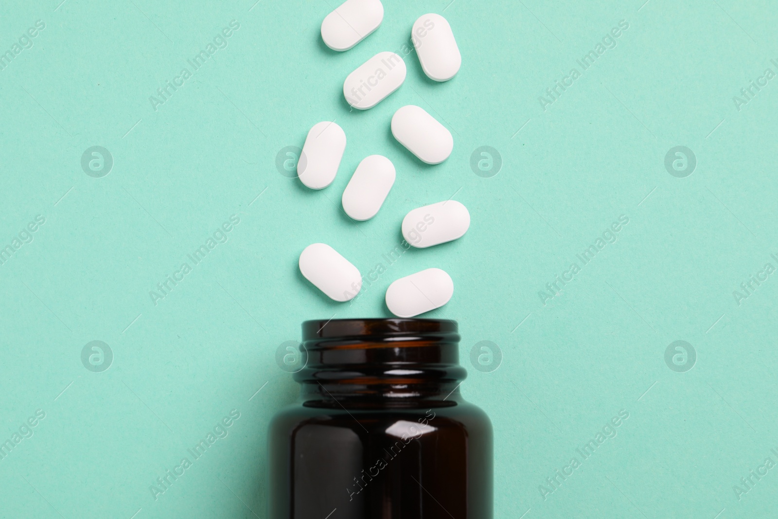 Photo of Plastic medical bottle with many pills on turquoise background, flat lay