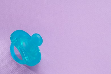 Photo of New baby pacifier on purple background, top view. Space for text