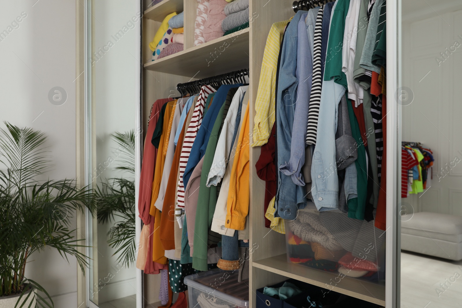 Photo of Wardrobe closet with different stylish clothes and home stuff in room. Fast fashion