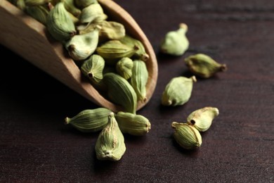 Scoop with dry cardamom pods on wooden table, closeup