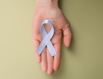 Photo of International Psoriasis Day. Woman with light blue ribbon as symbol of support on green background, top view. Space for text