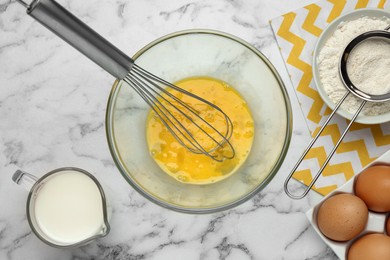 Photo of Whisked eggs and other ingredients on white marble table, flat lay