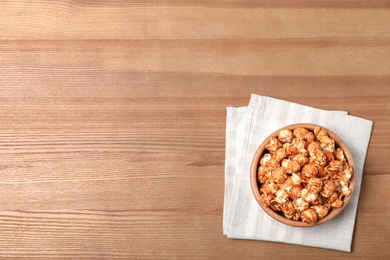 Photo of Bowl with caramel popcorn on wooden background, top view. Space for text