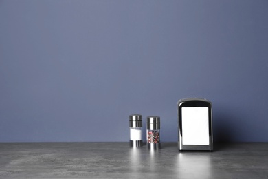 Photo of Napkin holder with salt and pepper shakers on table against color background. Space for text