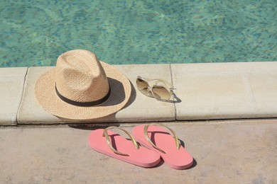Photo of Stylish hat, flip flops and sunglasses near outdoor swimming pool on sunny day. Beach accessories