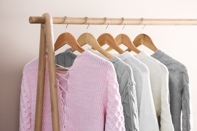 Photo of Collection of warm sweaters hanging on rack near light wall