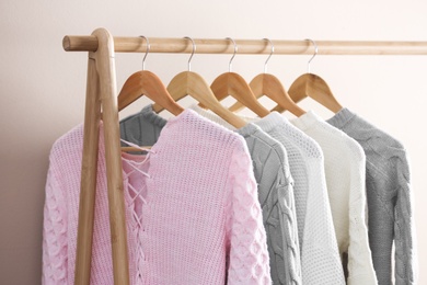 Collection of warm sweaters hanging on rack near light wall