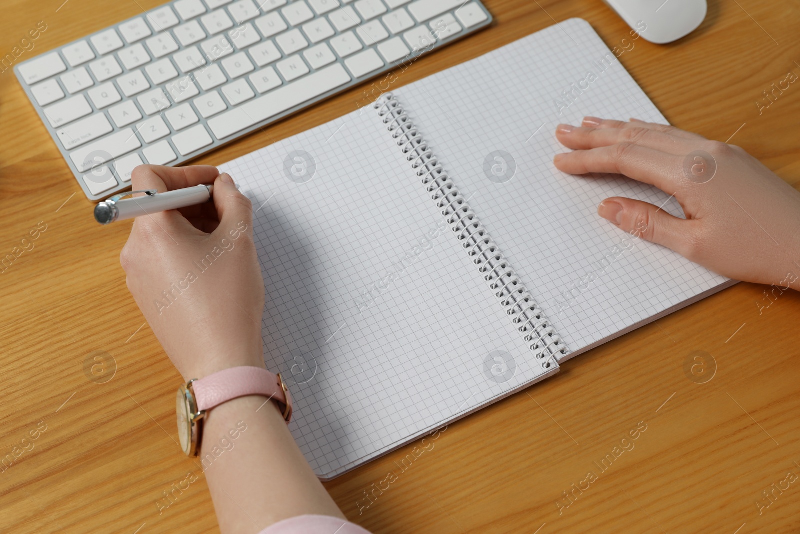 Photo of Left-handed woman writing in notebook at wooden desk, closeup