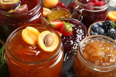 Photo of Jars with different jams and fresh fruits on table, closeup