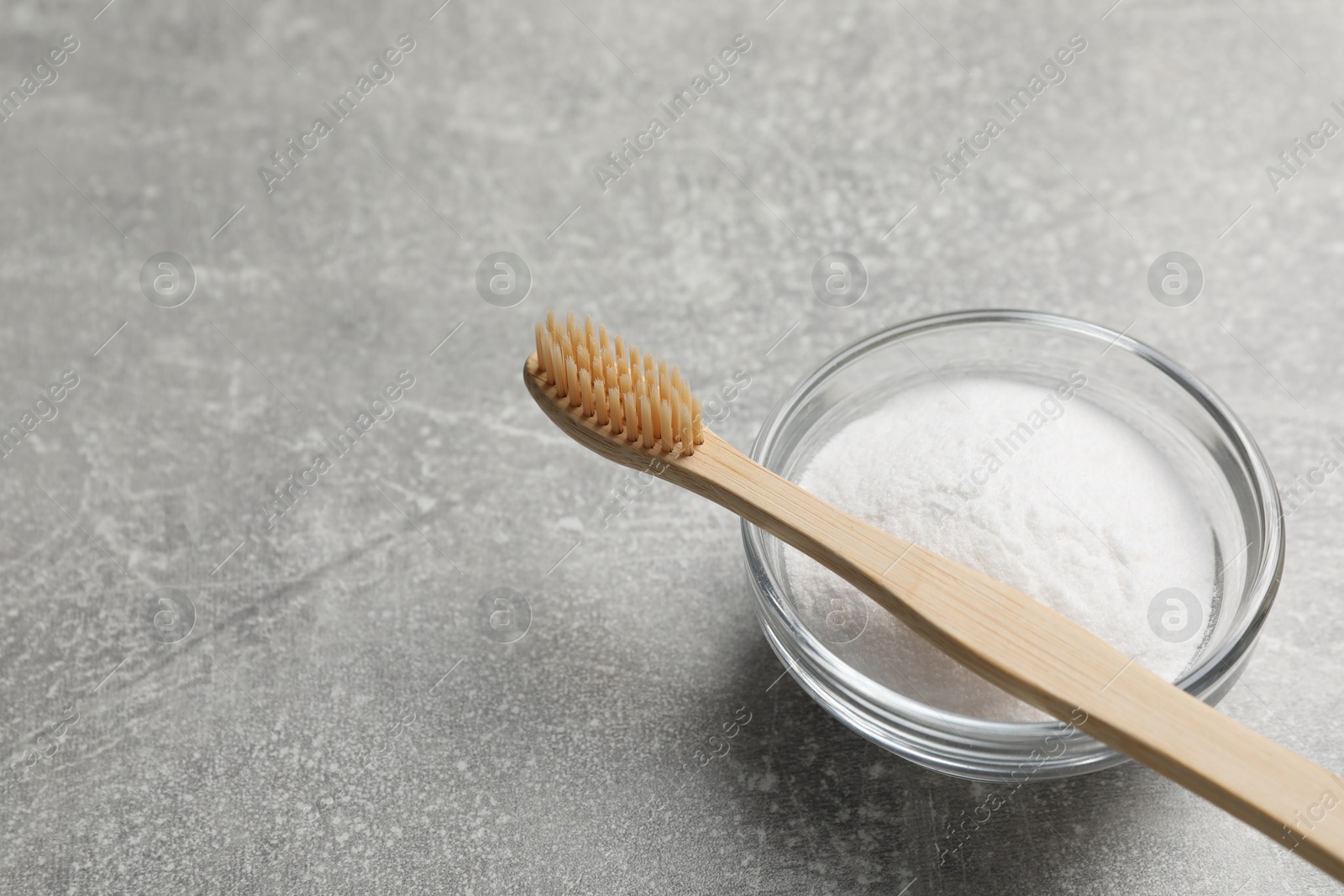 Photo of Bamboo toothbrush and bowl of baking soda on grey table, space for text