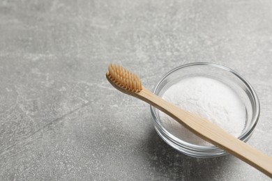 Bamboo toothbrush and bowl of baking soda on grey table, space for text