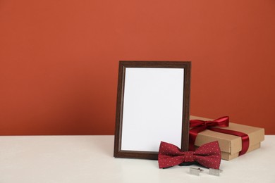 Photo of Happy Father's Day. Empty frame, bow tie, cufflinks and gift box on white table. Space for text