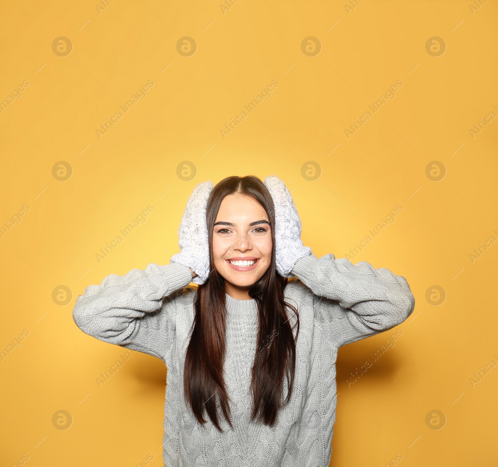 Image of Happy young woman wearing warm sweater and mittens on yellow background