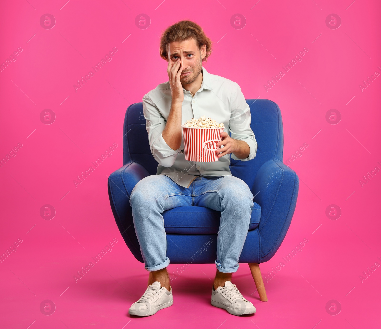 Photo of Emotional man with popcorn sitting in armchair during cinema show on color background