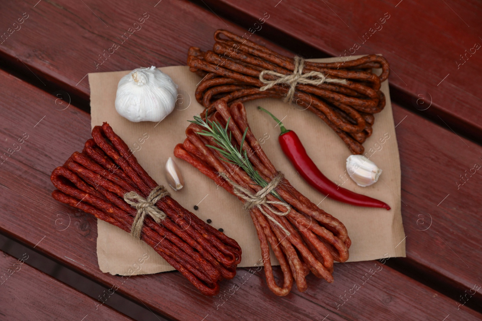 Photo of Bundles of delicious kabanosy with rosemary, peppercorn, garlic and chilli on wooden table, top view