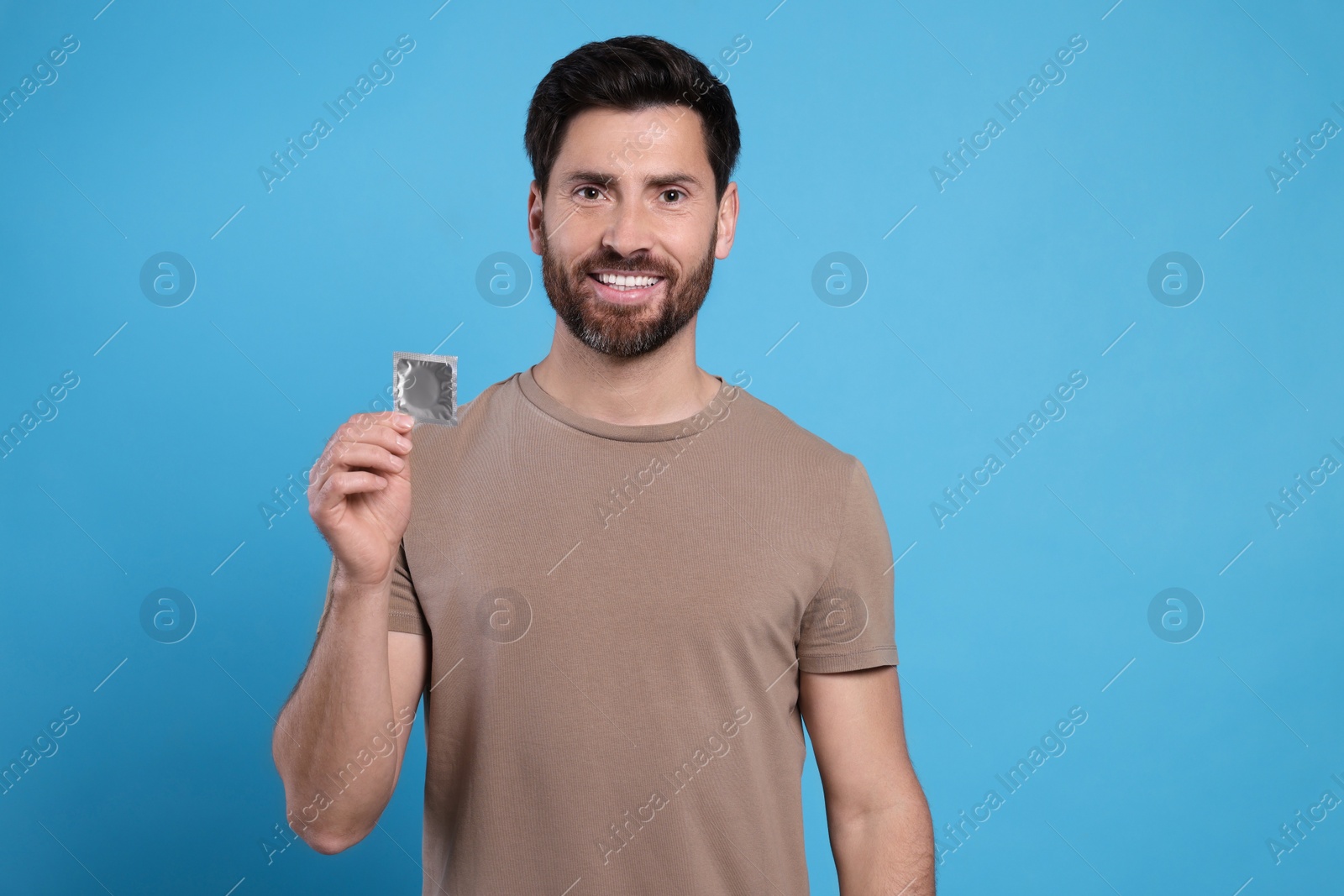 Photo of Happy man holding condom on light blue background, space for text. Safe sex