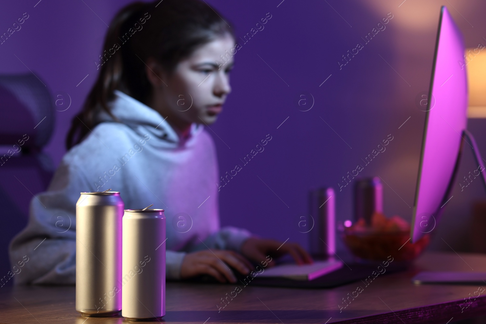 Photo of Girl playing computer game at home, focus on cans with energy drink