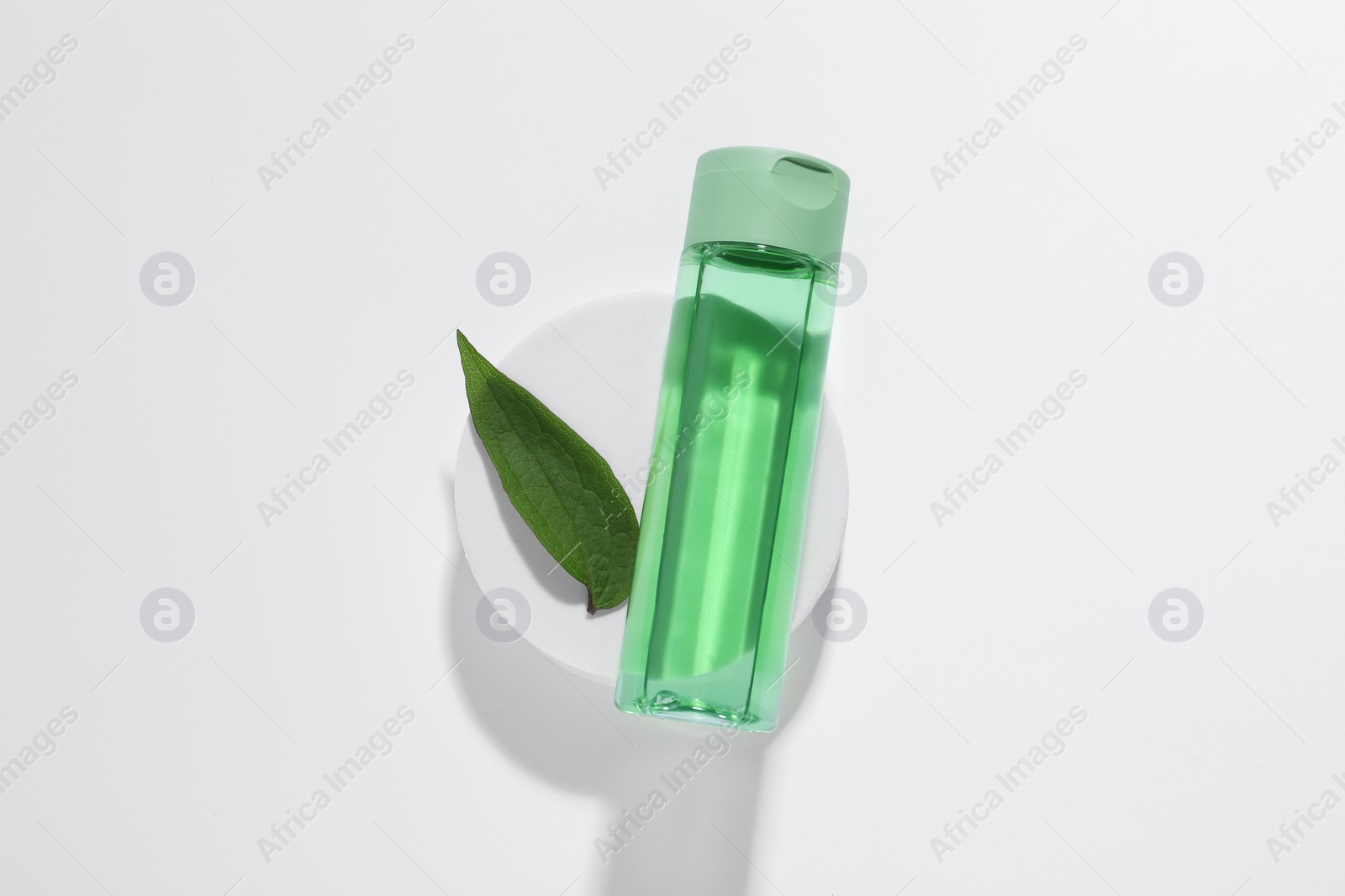 Photo of Bottle of cosmetic product, green leaf and podium on white background, top view