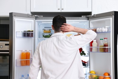 Man near refrigerator in kitchen at home, back view