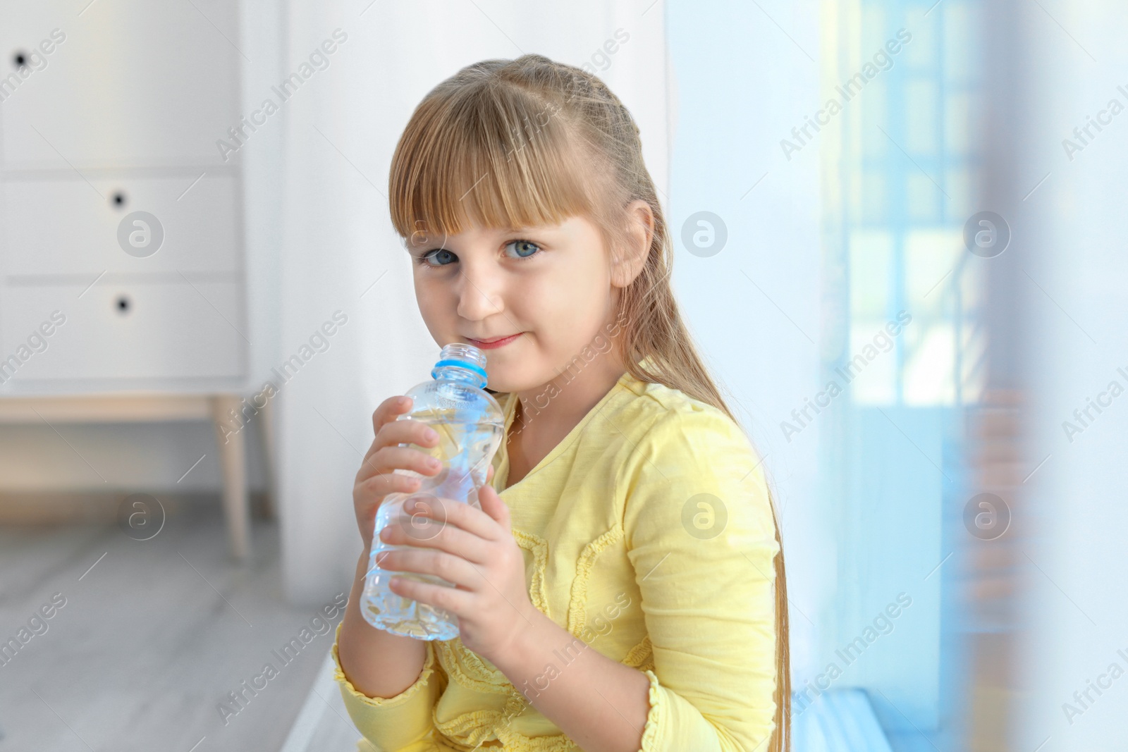 Photo of Cute little girl holding bottle with water indoors