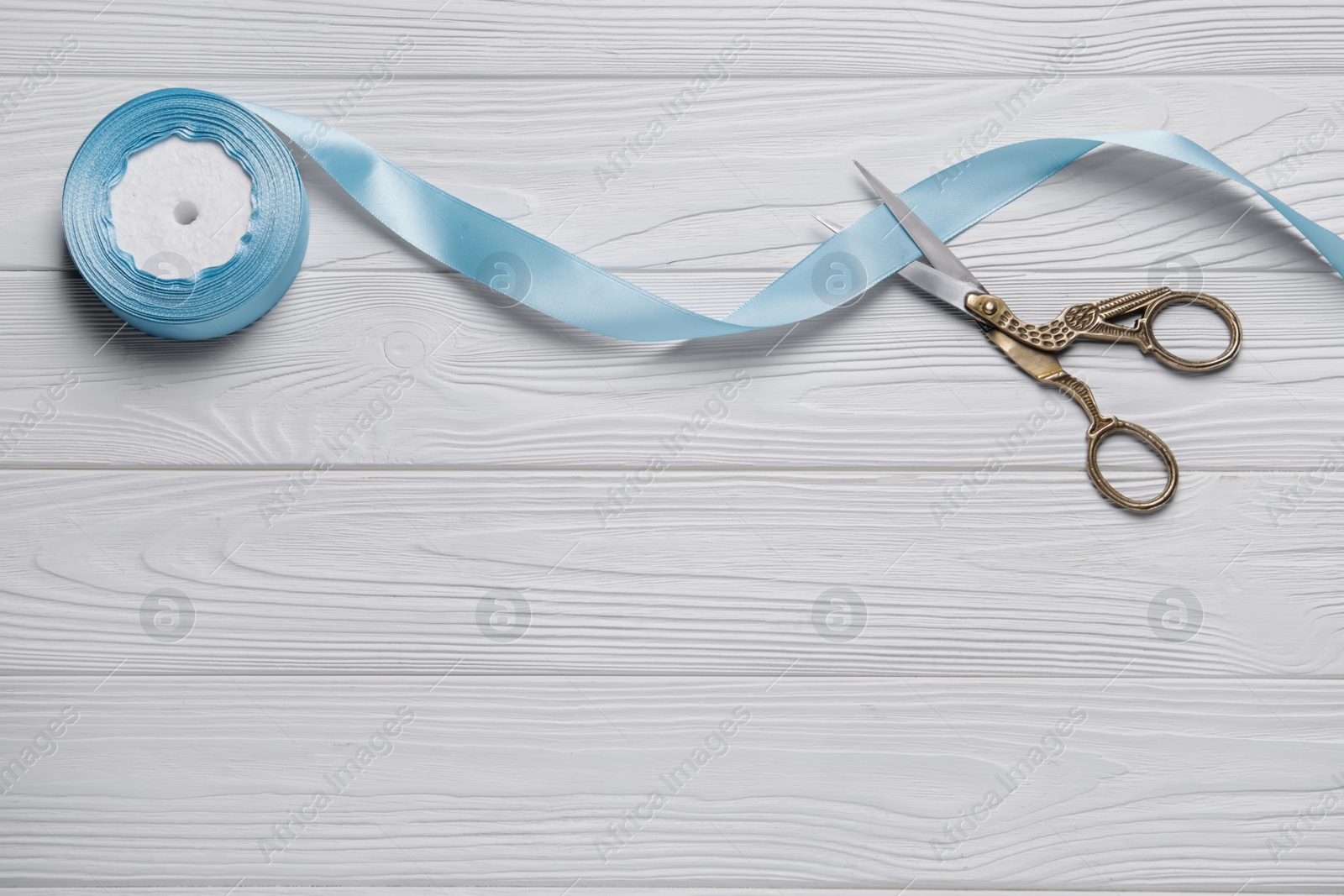 Photo of Pair of scissors with light blue satin ribbon on white wooden table, flat lay. Space for text