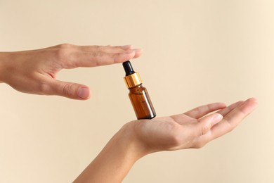 Woman with bottle of cosmetic serum on beige background, closeup