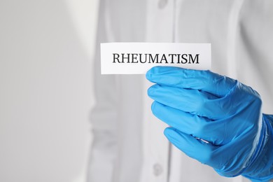 Doctor in glove holding sheet of paper with word Rheumatism, closeup