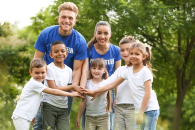 Group of kids joining hands with volunteers in park