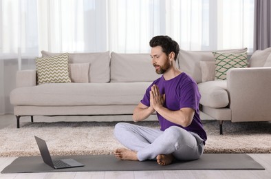 Man meditating near laptop at home, space for text