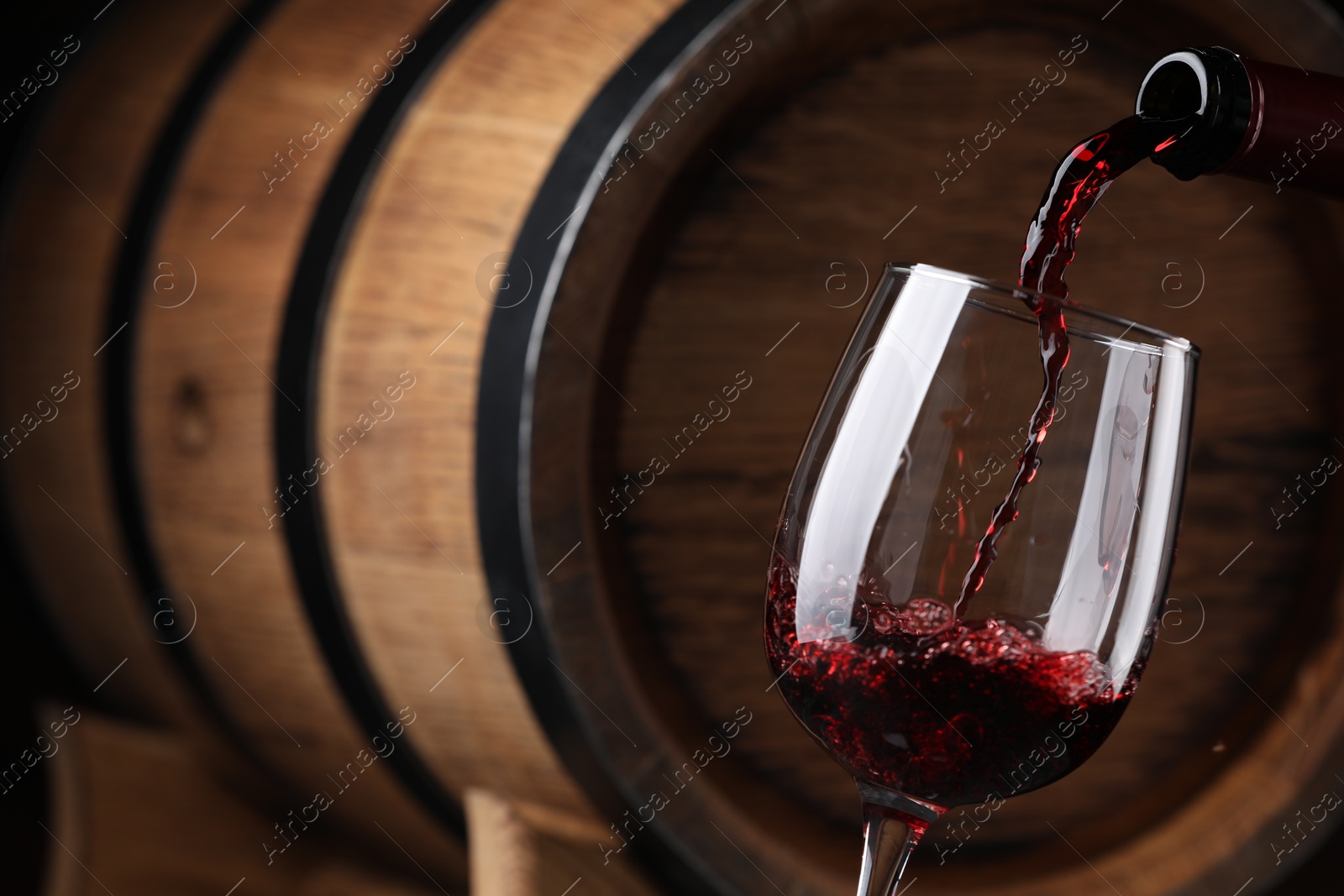 Photo of Pouring delicious wine into glass against wooden barrel, closeup