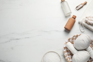 Flat lay composition with herbal massage bags and other spa products on white marble table. Space for text