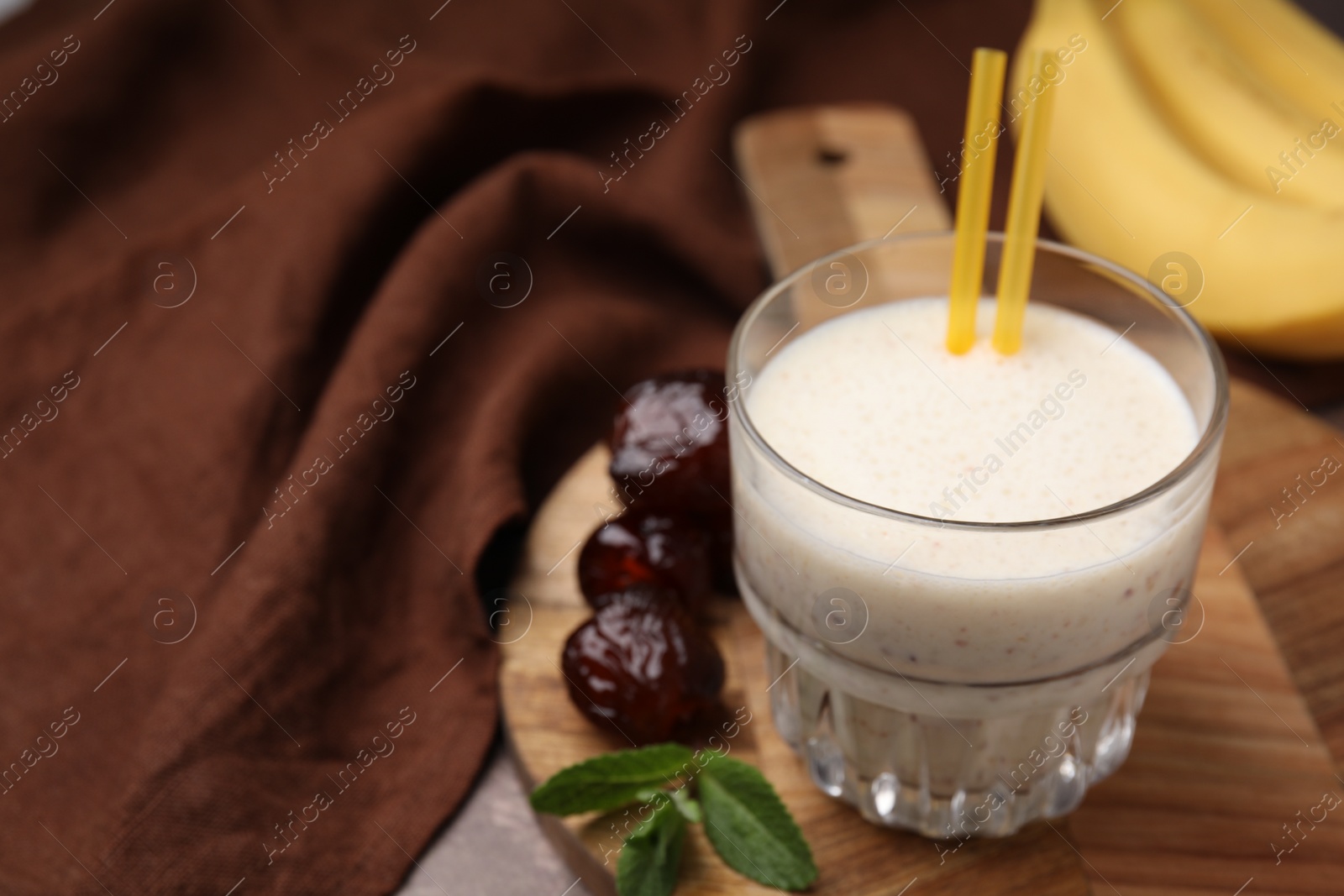 Photo of Glass of delicious date smoothie, mint and dried fruits on wooden board, closeup. Space for text