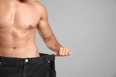 Young man with slim body in old big size jeans on grey background, closeup view. Space for text