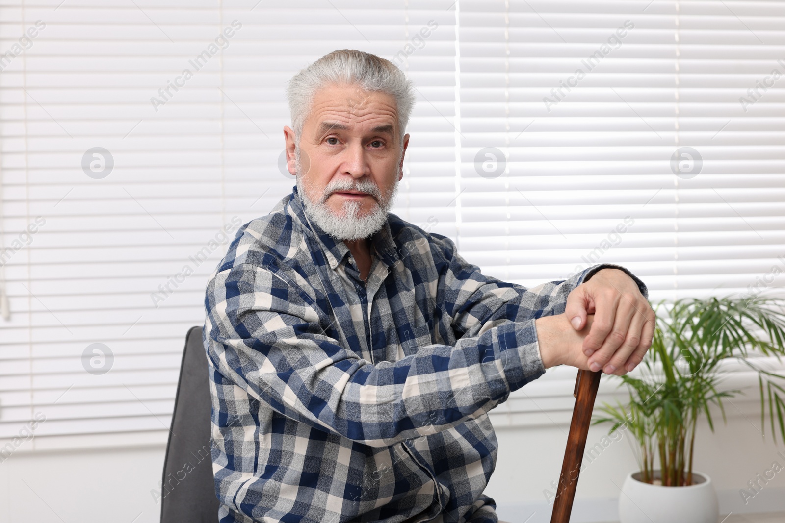 Photo of Senior man with walking cane sitting on armchair at home