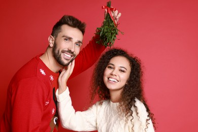 Photo of Portrait of lovely couple under mistletoe bunch on red background