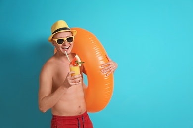 Shirtless man with inflatable ring and glass of cocktail on color background